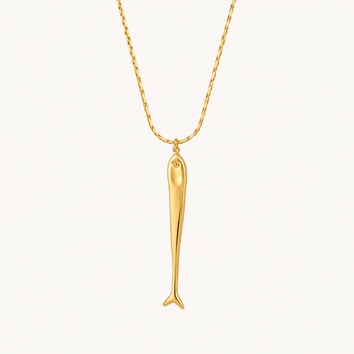 Pescara long fish pendant necklace in polished gold on a warm ivory background.