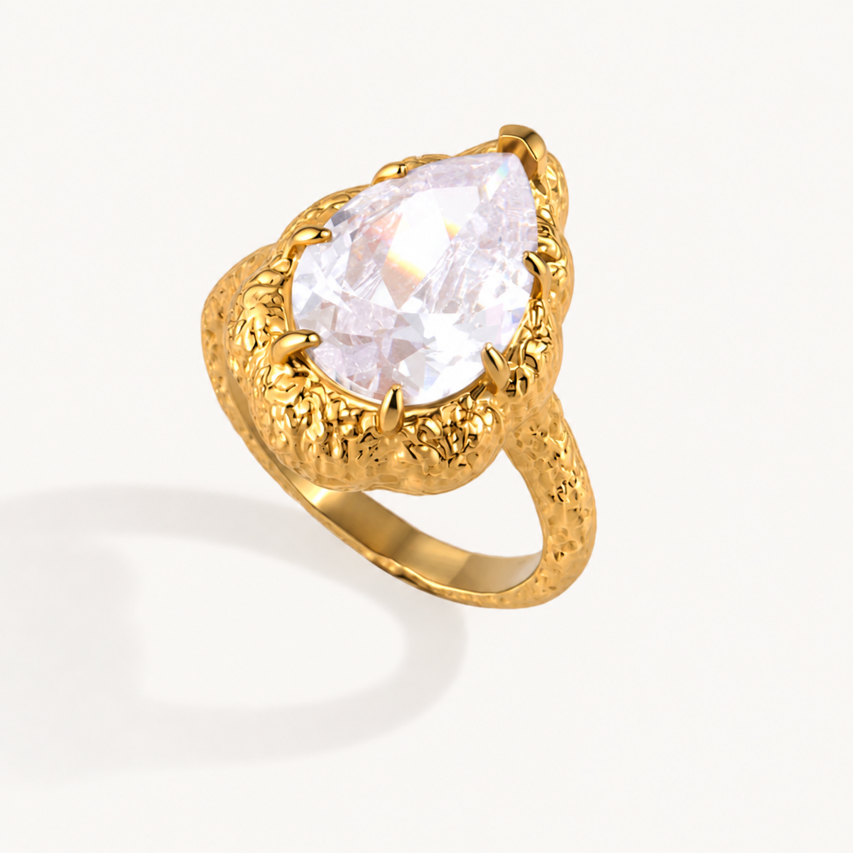 Serafina textured gold ring with a clear pear-cut zircon on a warm ivory background