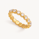 Lucetta gold textured eternity ring with clear bezel-set zircon stones on a warm ivory background.
