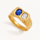 Textured gold ring with cobalt blue and clear oval zircon stones on warm ivory